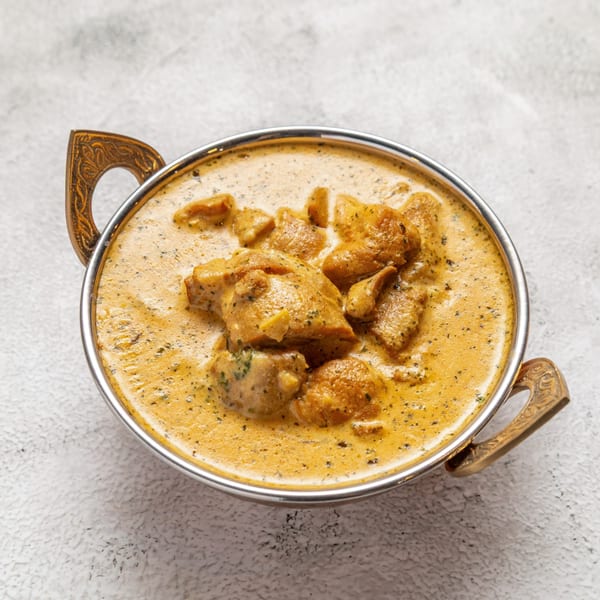 Nepalese chicken curry in a decorative metal bowl with ornate handles on a light background.