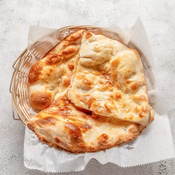 Golden brown naan bread, fresh from the oven, served in a woven basket lined with parchment paper.