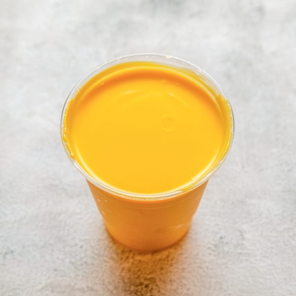 A vibrant yellow mango lassi in a clear plastic cup, viewed from above.