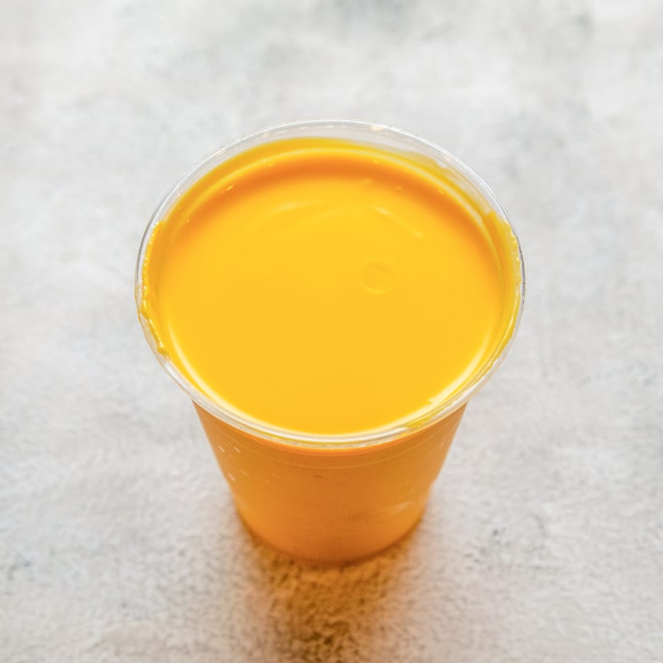 A vibrant yellow mango lassi in a clear plastic cup, viewed from above.