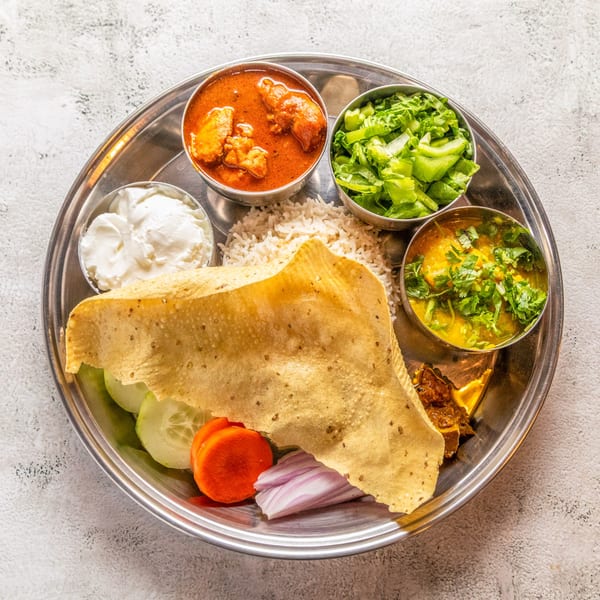 A Nepali thali with chicken curry, dal, rice, salad, yogurt, papad, and vegetables on a steel plate.