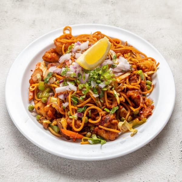 A plate of Nepalese chowmein with chicken, vegetables, red onions, cilantro, and a lemon wedge.