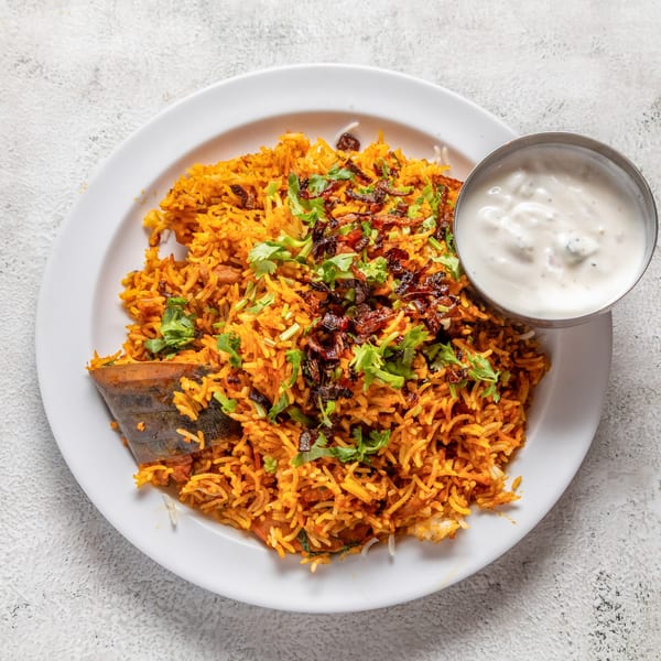 Nepalese chicken biryani with rice, herbs, and a side of raita on a white plate.